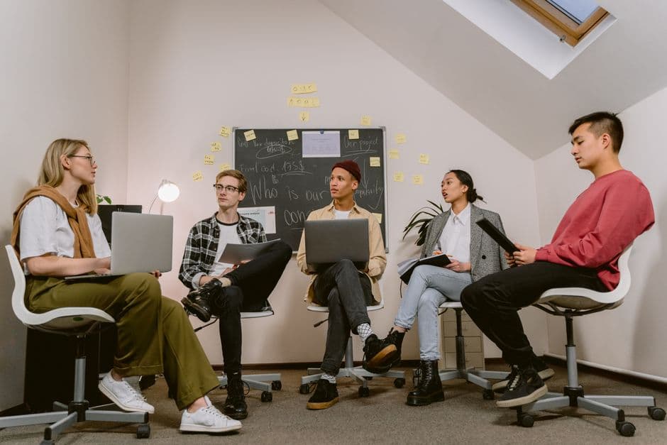 Young professionals engage in a collaborative meeting with laptops and a chalkboard focus.