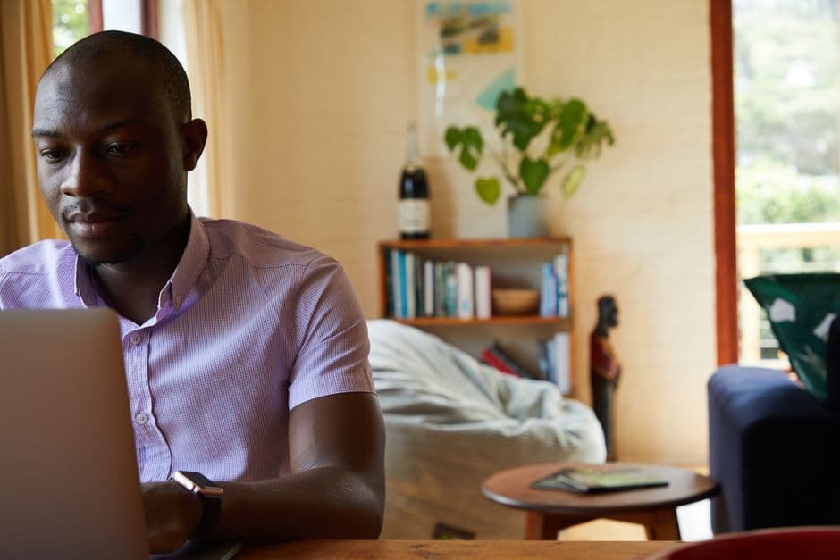 Concentrated African American man in formal clothes sitting at table and browsing netbook while working at home