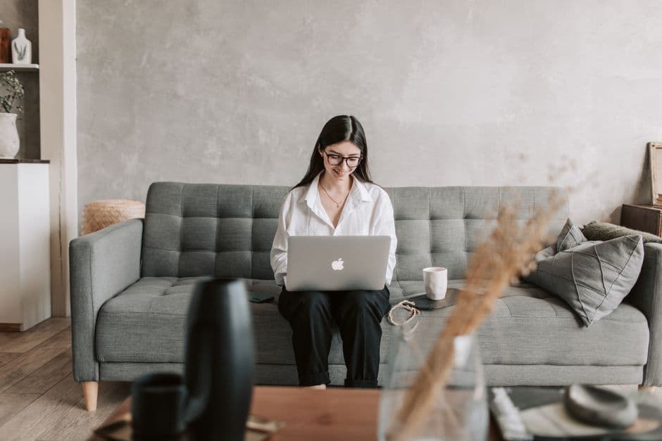 A woman works remotely on a laptop while sitting comfortably at home, exuding a modern and relaxed lifestyle.