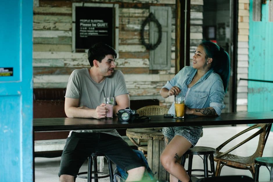 Positive multiracial couple drinking refreshing beverages while sitting at table with modern photo camera in light cafe on summer day
