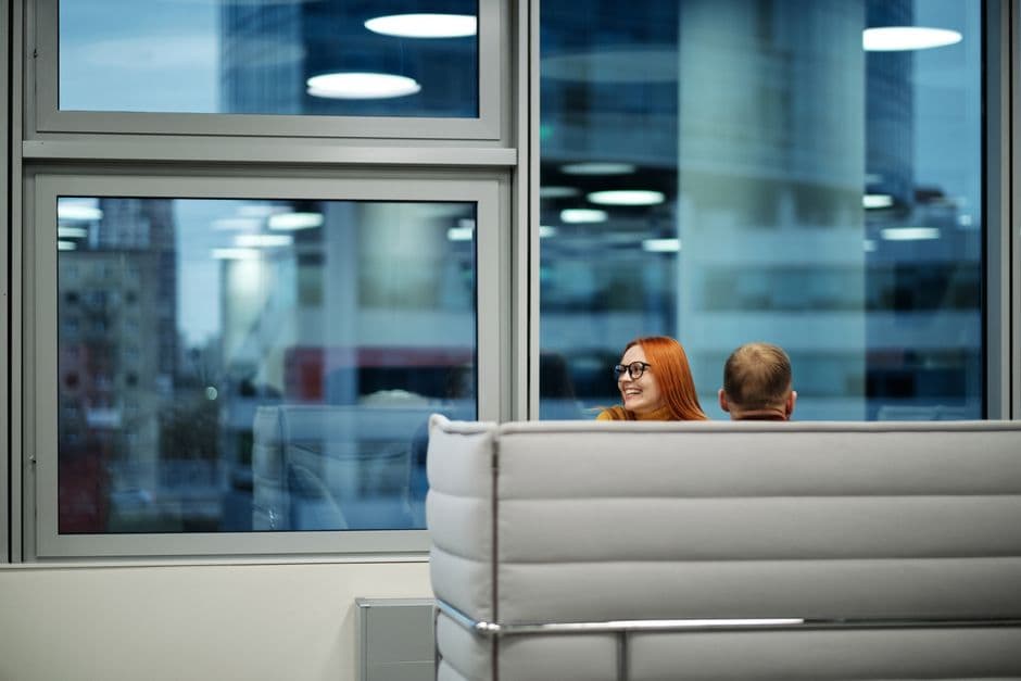 Colleagues enjoying a casual discussion in a spacious office lounge with large windows.