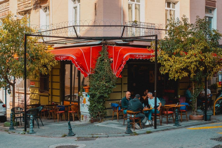 Relaxed outdoor seating at a European café on a city corner with vibrant red awning.