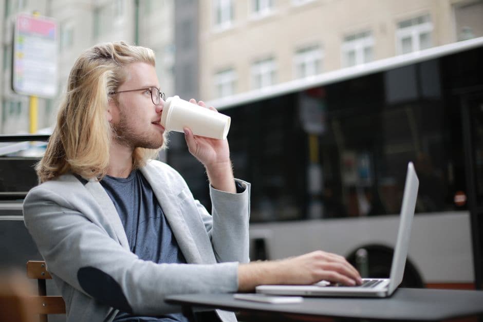 Young man working remotely on laptop while enjoying a coffee outdoors.